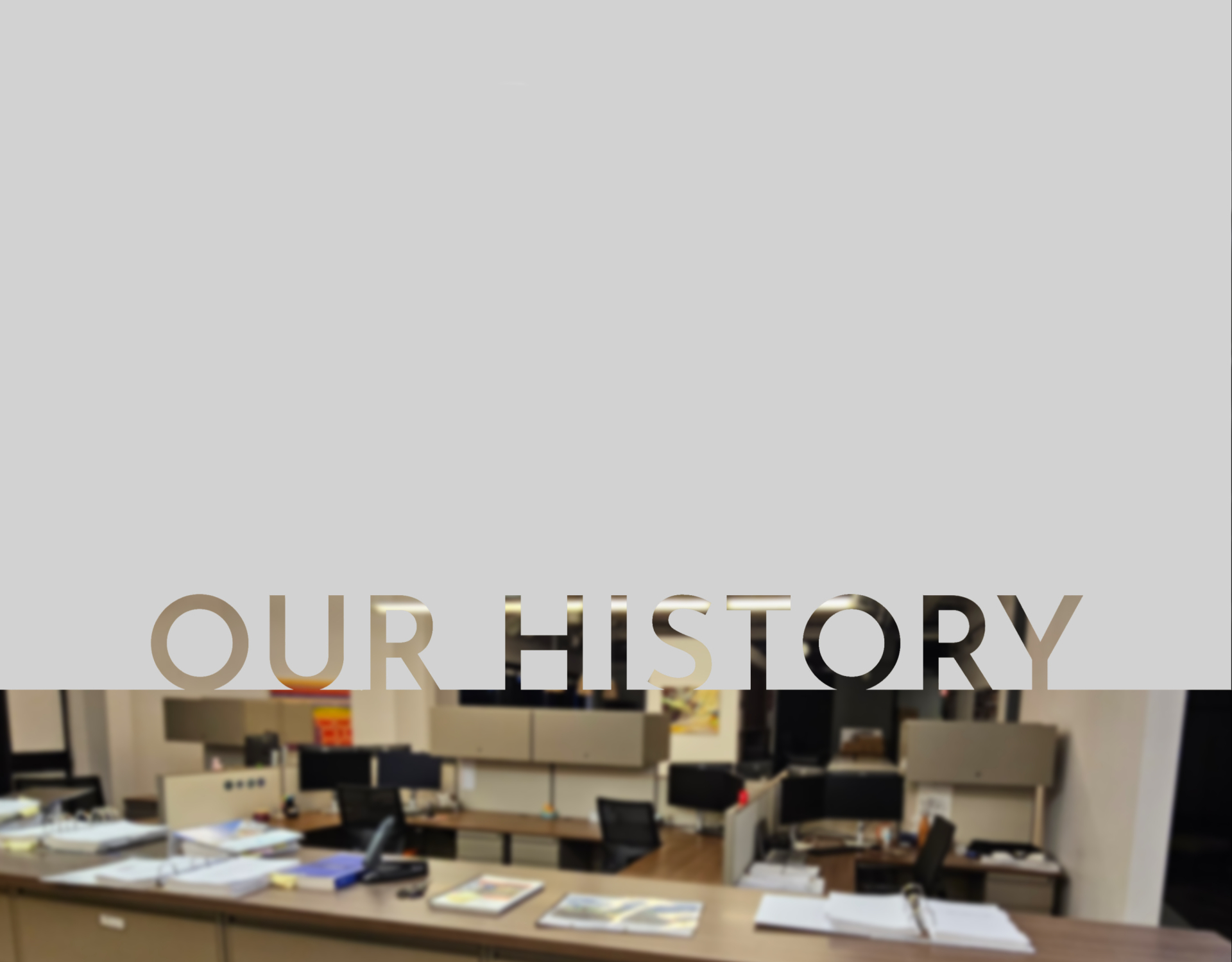 The words “OUR HISTORY” appear across the top of the image, overlaid on an office setting where several people stand and talk among cubicles, with plants and maps visible in the background.